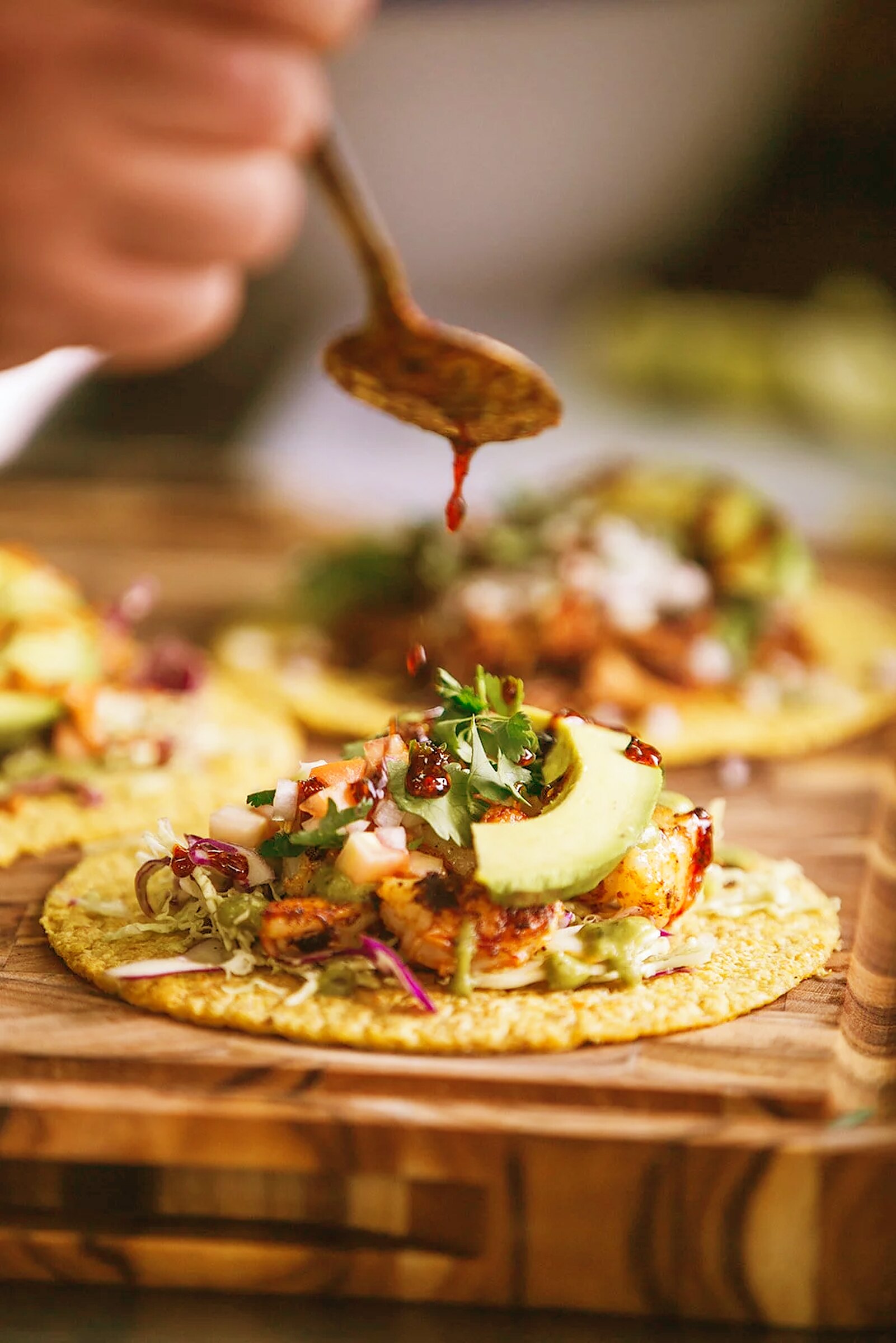 Salsa dripping from a spoon onto a prawn taco with avocado, pico de gallo and slaw